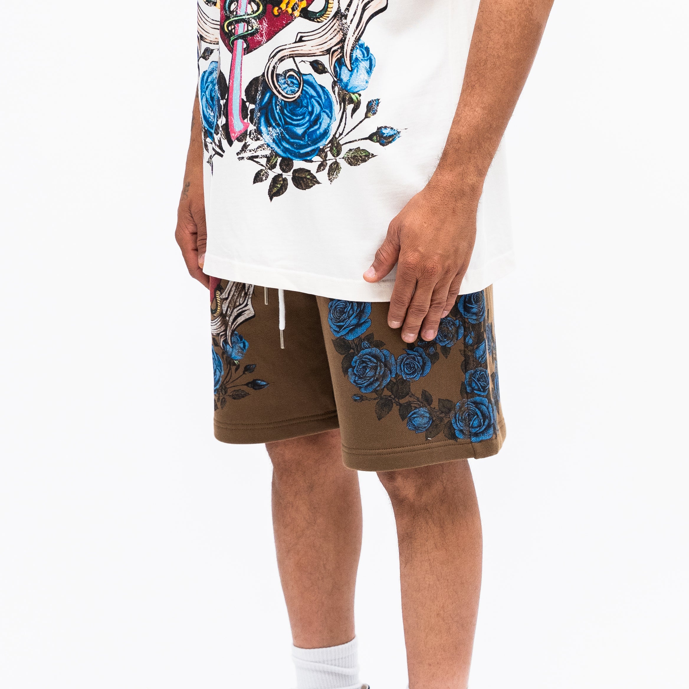 Person wearing a white t-shirt with a colorful design and brown shorts with blue floral patterns on a white background