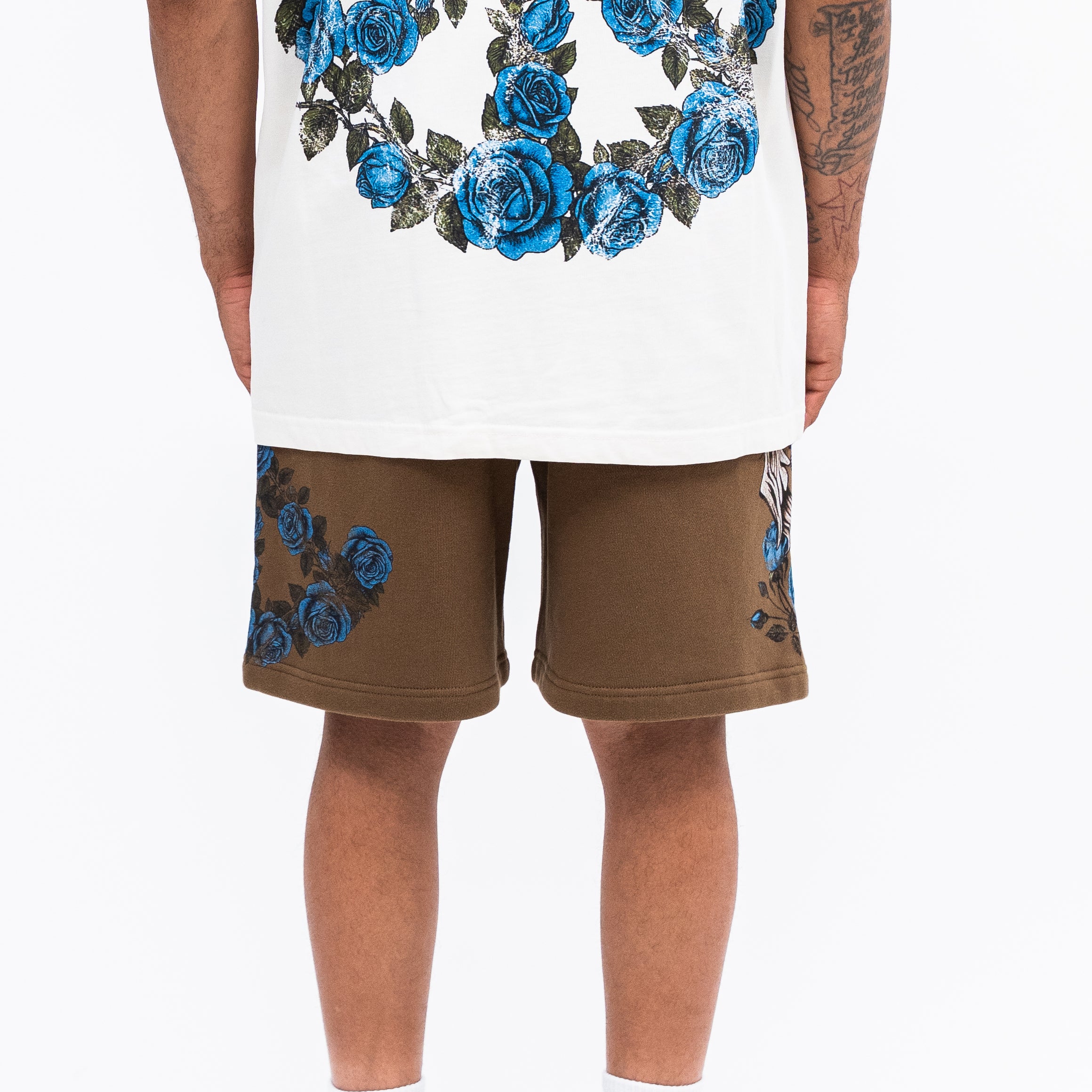Person wearing a white tank top with blue floral design and brown shorts with blue floral design on a white background