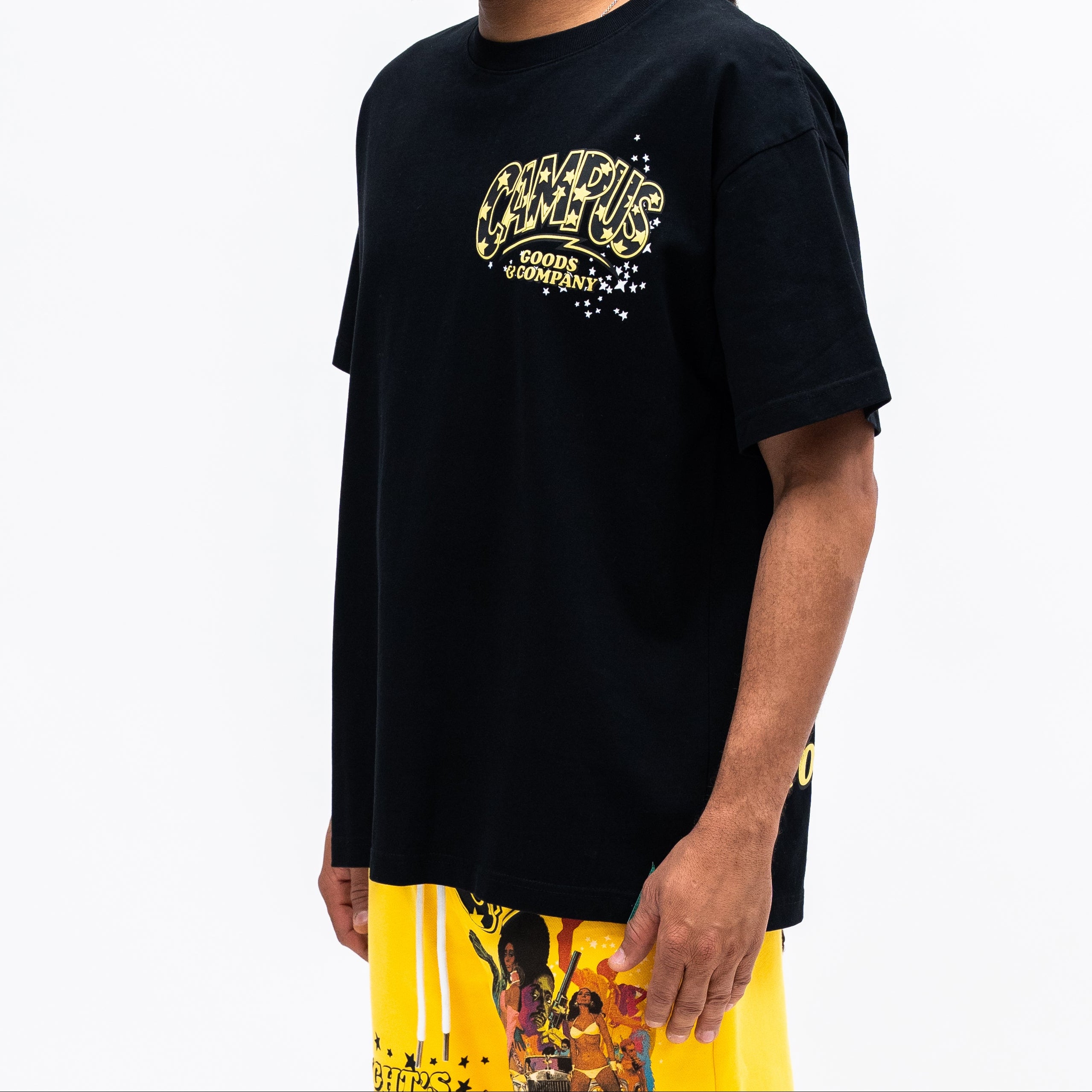 Person wearing a black t-shirt with yellow text and colorful pants on a white background