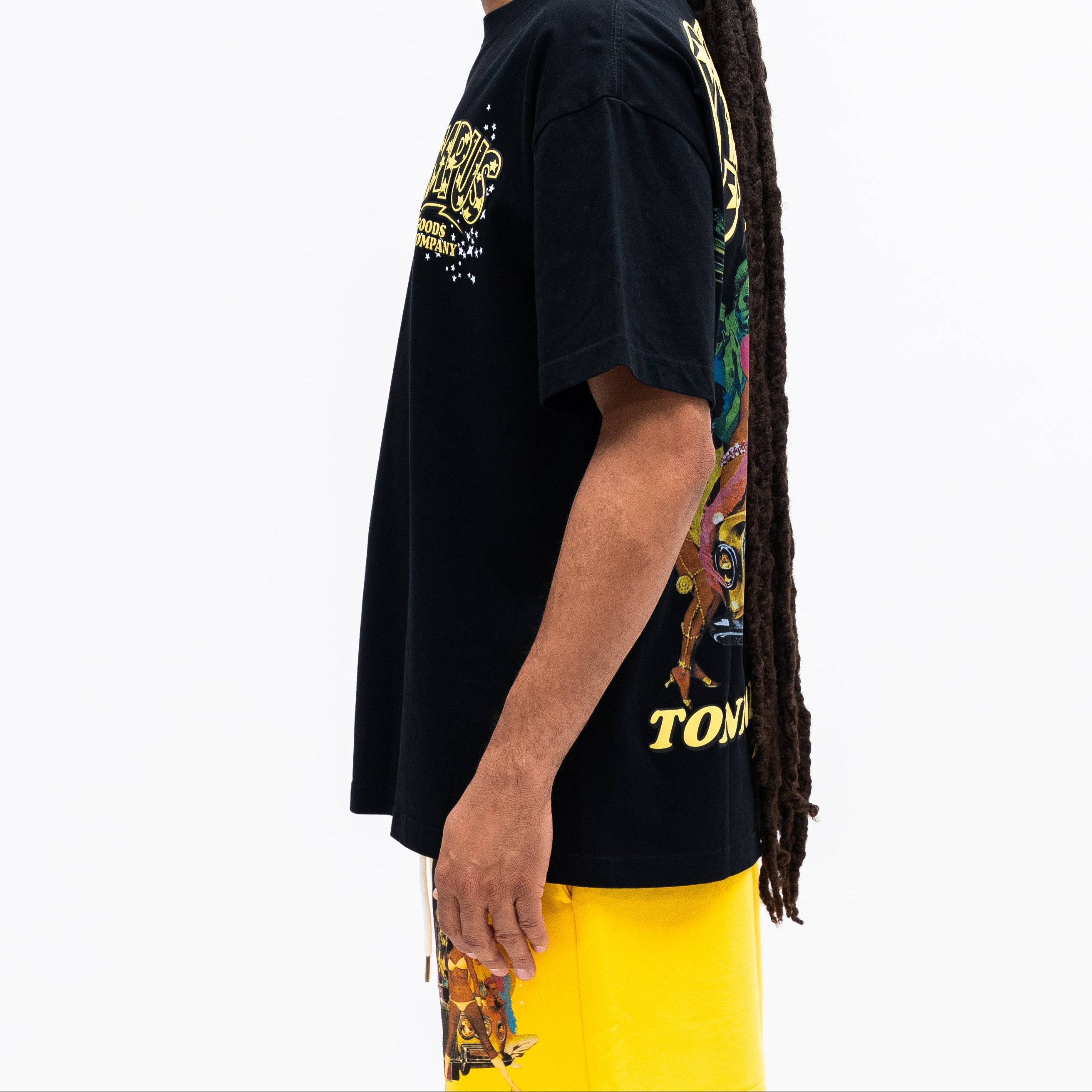Person wearing a black t-shirt with colorful designs and yellow pants on a white background