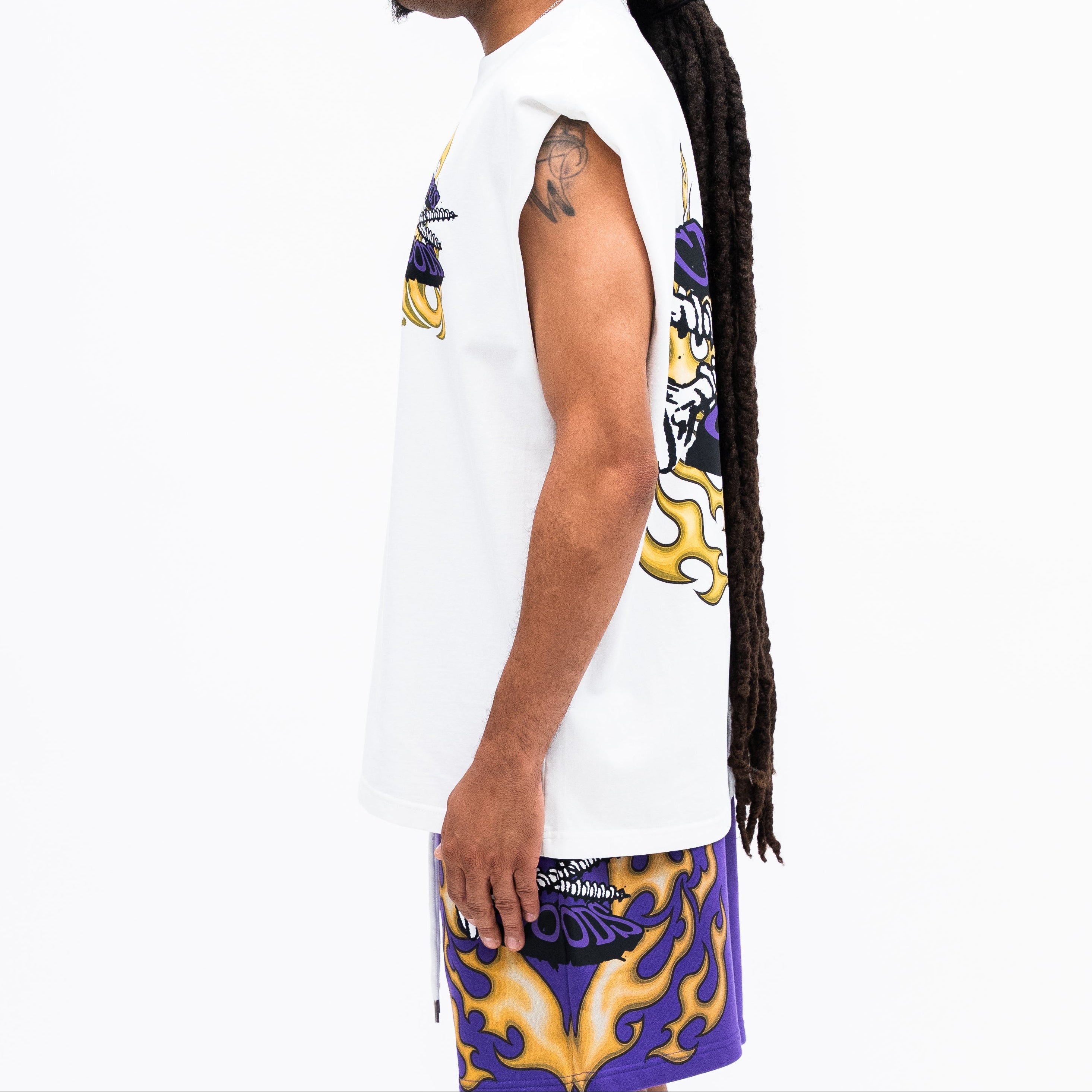 Person wearing a white sleeveless shirt with colorful graphics and purple shorts with yellow designs on a white background